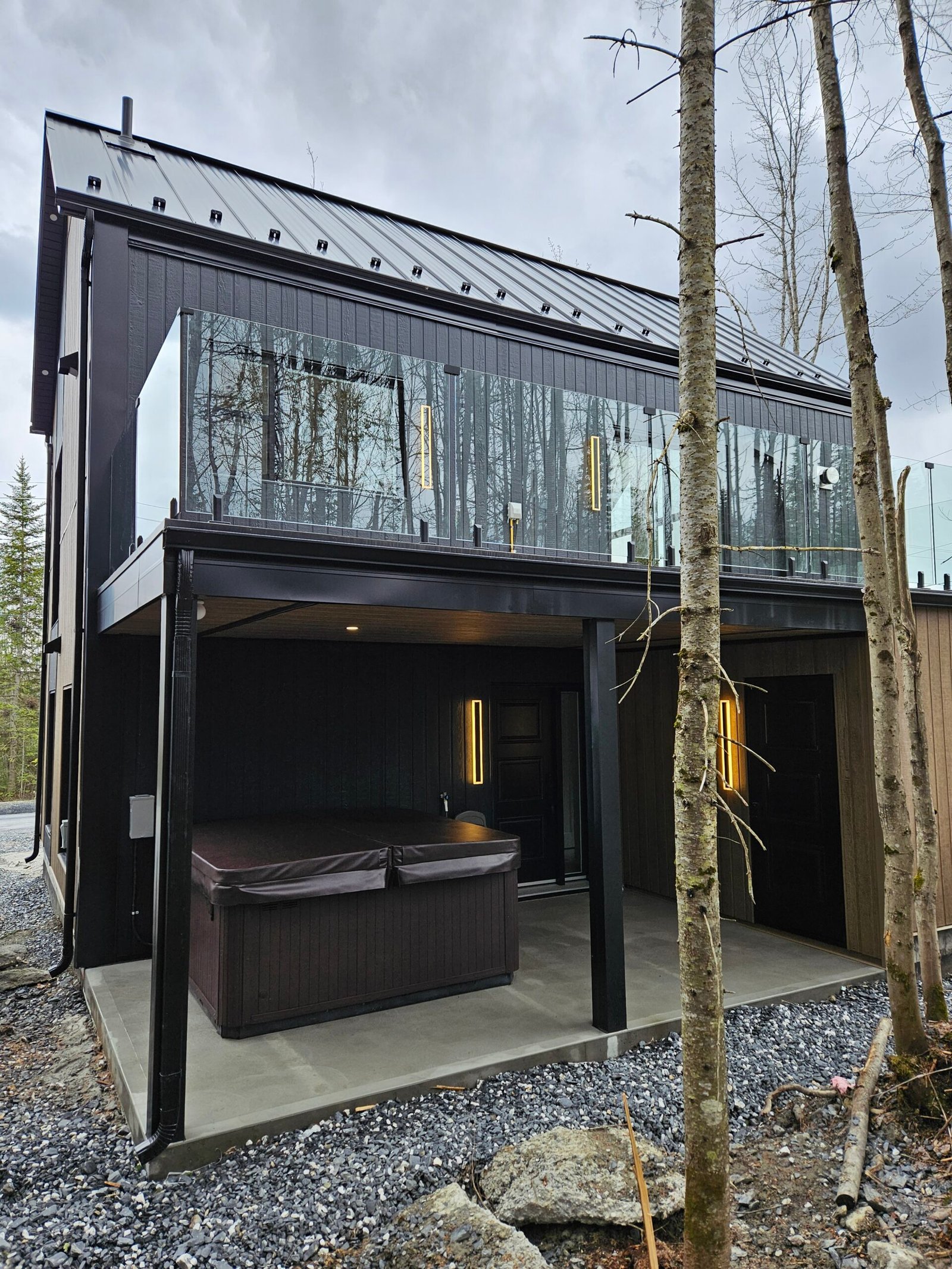 Vue côté gauche sur la terrasse, le spa et l'entrée du chalet Le Hygge Hytte